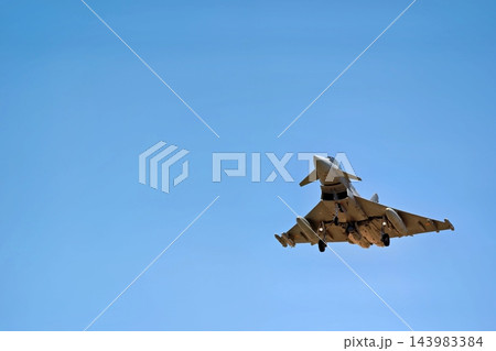Military fighter jet flying with landing gear extended in a clear blue sky, viewed from below during landing approach Military fighter jet flying with landing gear extended in a clear blue sky, viewed from below during landing approach 143983384