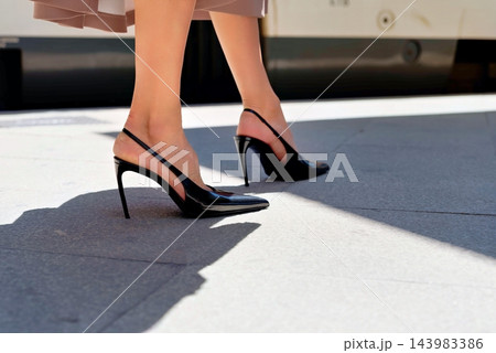 Woman wearing black slingback high heel shoes walking on a sunny urban pavement outdoors near a train platform Woman wearing black slingback high heel shoes walking on a sunny urban pavement outdoors near a train platform 143983386