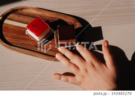 Child hand reaching for chocolate cake next to raspberry cheesecake on wooden board Child hand reaching for chocolate cake next to raspberry cheesecake on wooden board 143985270