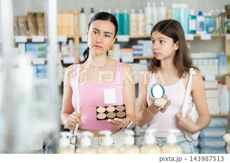 Positive family of woman and young girl buyers choosing cosmetics for makeup and beauty products in household chemicals store or pharmacy 143987513