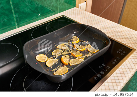 Lemon slices with rosemary in baking tray on induction cooktop, fresh citrus aromas, with lemon, slice, rosemary, herb detail, showing baking, tray, dish, kitchen context 143987514