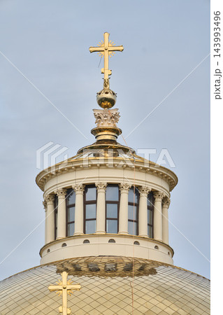Golden cross on ornate church tower above gilded sphere and domed cupola, featuring stone masonry and decorative finials against clear blue sky 143993496