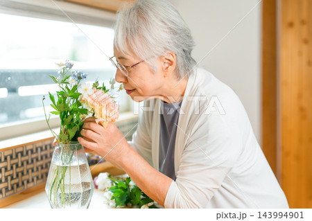 花瓶に顔を寄せて花の香りを楽しむシニア女性 花瓶に顔を寄せて花の香りを楽しむシニア女性 143994901