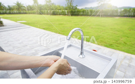 Woman washing hands with clean running tap water at an outdoor sink beside a green lawn on a sunny day, promoting personal hygiene, sanitation, health protection and responsible water use. Woman washing hands with clean running tap water at an outdoor sink beside a green lawn on a sunny day, promoting personal hygiene, sanitation, health protection and responsible water use. 143996759