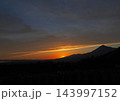 磐梯山の麓に夕日が落ちかける寸前。山のシルエットとオレンジ色に輝く雲の線が印象的で綺麗だ。 143997152