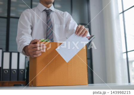 Business professional holding resignation letter and packed of personal belongings in cardboard on a desk. Concept of job resignation or termination. 143998215