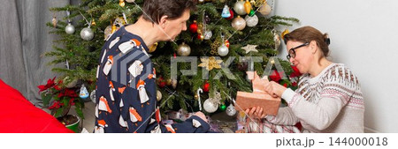 On Christmas Day, a 52-year-old couple spends time together near a decorated tree. They exchange gifts and celebrate the holiday in their cozy home setting filled with decorations On Christmas Day, a 52-year-old couple spends time together near a decorated tree. They exchange gifts and celebrate the holiday in their cozy home setting filled with decorations 144000018