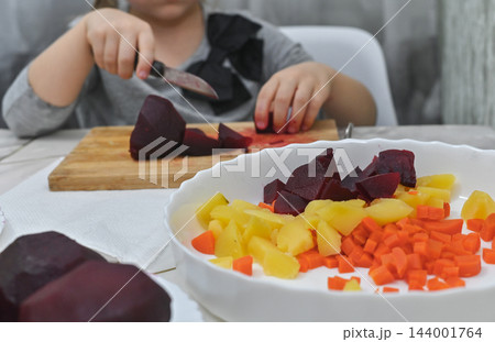 Little girl is cutting beetroot for salad using kitchen knife. 144001764