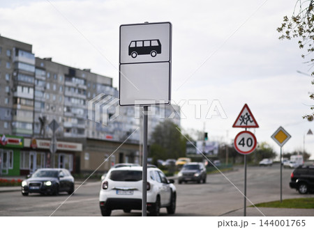 Bus stop sign stands along urban street with vehicles and residential buildings. Bus stop sign stands along urban street with vehicles and residential buildings. 144001765