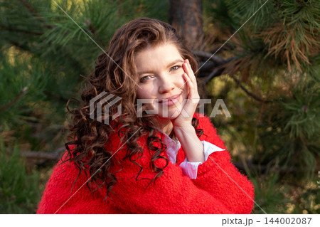 Smiling Curly Haired Woman Resting Hand on Face Outdoors 144002087