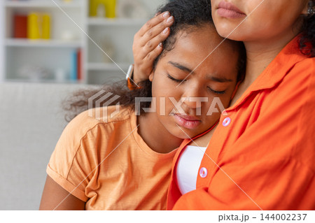 Black daughter is resting her head against her mothers chest at home 144002237