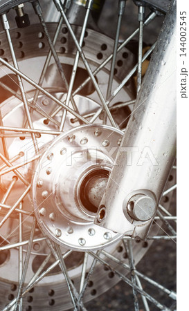 Close up detail of motorcycle front wheel, showing metal spokes, disc brake rotor, and lower fork with water droplets on surface, vertical composition, focus on engineering. 144002545