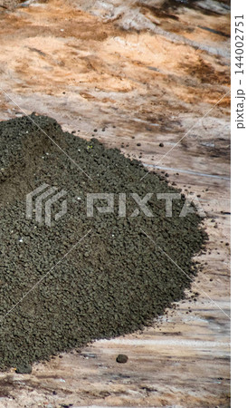 Pile of dark granular material rests on dry textured ground, showing aggregate composition for construction purposes, featuring small stones and fine particles, useful for building projects vertical Pile of dark granular material rests on dry textured ground, showing aggregate composition for construction purposes, featuring small stones and fine particles, useful for building projects vertical 144002751