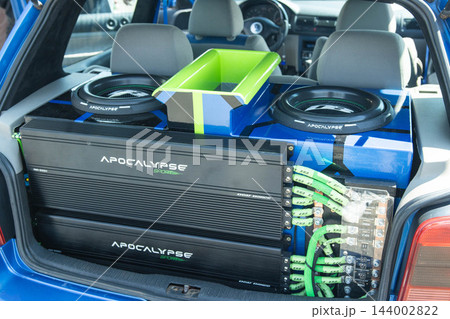 Car trunk interior showcases custom high-performance automotive audio system, featuring large subwoofers, power amplifiers, intricate neon green wiring, and specialized sound equipment. Car trunk interior showcases custom high-performance automotive audio system, featuring large subwoofers, power amplifiers, intricate neon green wiring, and specialized sound equipment. 144002822