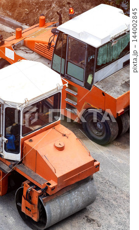 Orange asphalt paving roller and road construction machine on job site, heavy equipment compaction work on new road surface development, overhead view vertical photo Orange asphalt paving roller and road construction machine on job site, heavy equipment compaction work on new road surface development, overhead view vertical photo 144002845