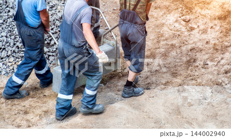 Construction workers installing concrete road curbing element on street building site. Heavy manual labor of three men lifting kerb stone for urban infrastructure development project, copy space 144002940