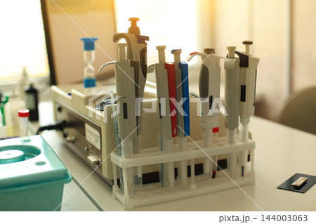 Row of precision automatic pipettes and dispensers in laboratory rack on desk beside centrifuge during medical diagnostic procedures for blood collection from finger. Row of precision automatic pipettes and dispensers in laboratory rack on desk beside centrifuge during medical diagnostic procedures for blood collection from finger. 144003063