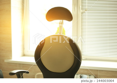 Back view of empty medical examination chair in modern otolaryngologist laboratory room beside bright window with venetian blinds during sunny day in hospital clinic 144003064