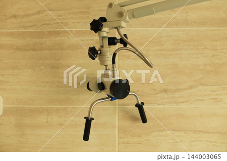 modern professional otolaryngologist laboratory examination microscope mounted on adjustable articulated metal arm against beige marble tile wall in medical clinic modern professional otolaryngologist laboratory examination microscope mounted on adjustable articulated metal arm against beige marble tile wall in medical clinic 144003065