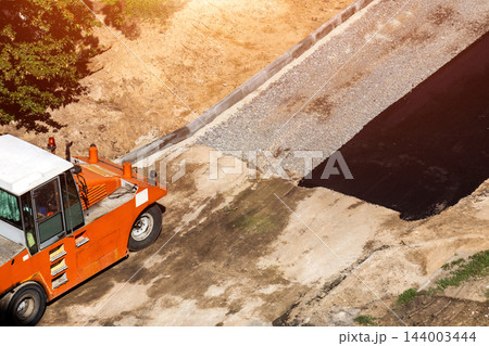 Aerial view of asphalt paver machine on construction site, new road surface preparation, laying fresh black asphalt, gravel foundation with curbstone, sunny day outdoor scene. Copy space 144003444
