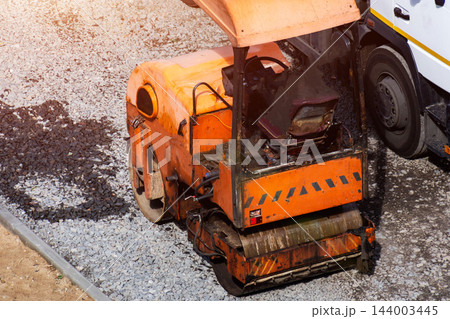 Construction machinery orange asphalt paving roller on gravel surface preparing road base bright sunlight work progress aerial view no people present 144003445