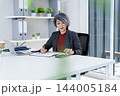 Businesswoman Calculating Finances and Reviewing Charts at Office 144005184