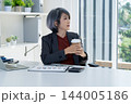 Businesswoman Taking a Coffee Break and Looking Out Window in Office 144005186