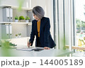 Businesswoman Standing at Desk Analyzing Financial Charts 144005189
