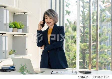 Businesswoman Standing and Talking on Smartphone in Office 144005192