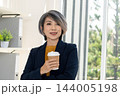 Businesswoman Enjoying Coffee Break by Office Window 144005198