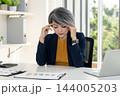 Stressed Businesswoman Rubbing Temples at Office Desk 144005203