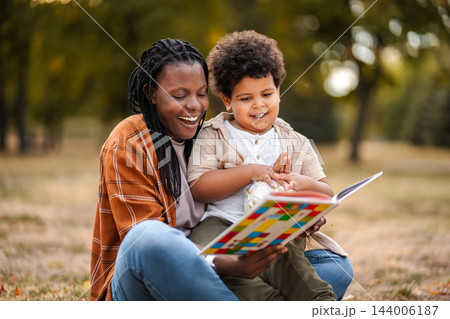 Mother son reading storybook enjoying family time outdoors Mother son reading storybook enjoying family time outdoors 144006187