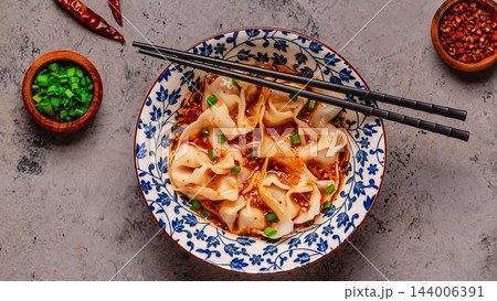 Wontons are placed in a bowl with spicy sauce. 144006391