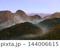 Autumn forested hills and rugged alpine peaks emerge through mist in golden morning light 144006615