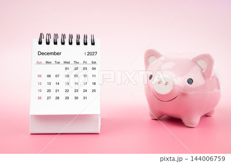 Desk calendar for December 2027 and pink piggy bank on pink background. Desk calendar for December 2027 and pink piggy bank on pink background. 144006759