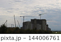 Against the backdrop of a gloomy sky, the reinforced concrete frameworks of multi-story buildings are being erected. Several tower cranes and mobile cranes are at work, constructing a new residential  144006761