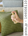 Close up of hand using spray bottle to freshen decorative cushion on sofa 144008110