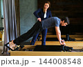 Personal trainer coaching a controlled reformer plank - wide view 144008548