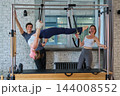 Personal trainer coaching two clients on Cadillac equipment - wide view 144008552