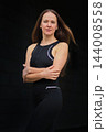 A woman in black sportswear poses with her arms crossed against a dark wall 144008558