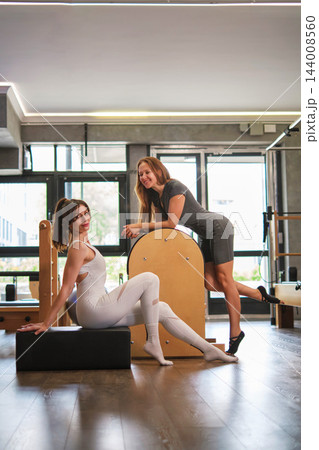 Two women beside Pilates equipment in a bright studio 144008560