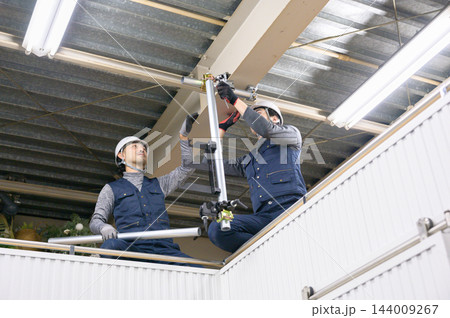 屋内の建設現場で協力して足場の単管パイプを組み立てる男性作業員2人 屋内の建設現場で協力して足場の単管パイプを組み立てる男性作業員2人 144009267