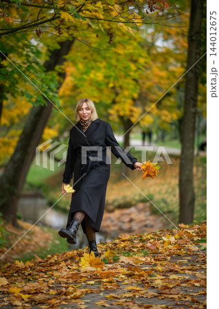 A smiling blonde woman in a long black coat 144012675