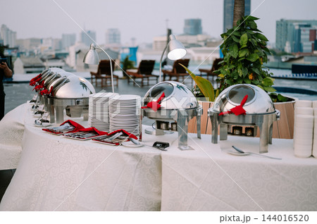 Outdoor Rooftop Buffet Setup with Chafing Dishes and City Skyline 144016520