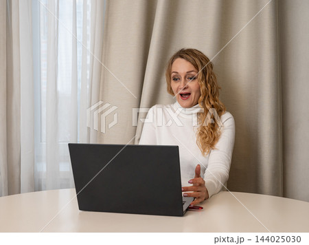 Surprised mature woman looking at laptop screen at home 144025030