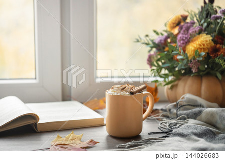 Cozy autumn reading with hot drink and open book by window Cozy autumn reading with hot drink and open book by window 144026683
