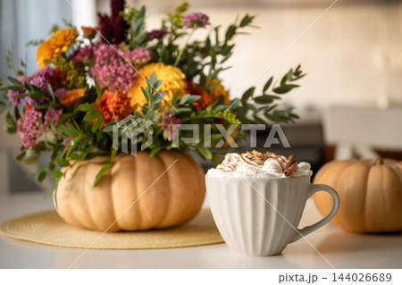 Coffee with whipped cream and cinnamon beside autumn flowers in pumpkin vase Coffee with whipped cream and cinnamon beside autumn flowers in pumpkin vase 144026689