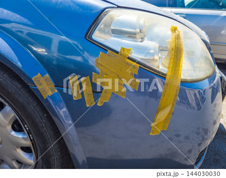 Close-up of blue car with yellow tape repair on fender and headlight Close-up of blue car with yellow tape repair on fender and headlight 144030030