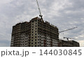 Construction of a multi-unit residential building using monolithic concrete. Tower cranes are positioned above and alongside the structure, facilitating the assembly of the floor slabs and the frame 144030845