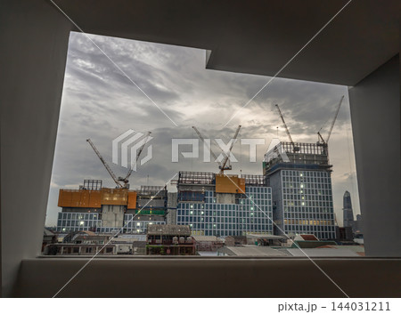 A panoramic view of a massive modern commercial complex under construction along Rama III Road, dramatically framed through a geometric concrete window opening. 144031211